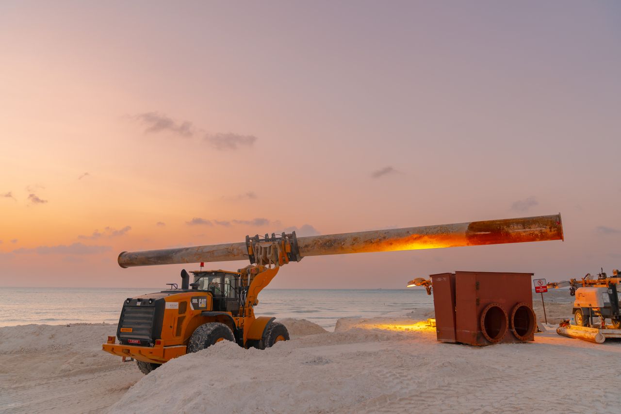 gallery-06 Dramatic view of beach construction site with heavy machinery at sunset.