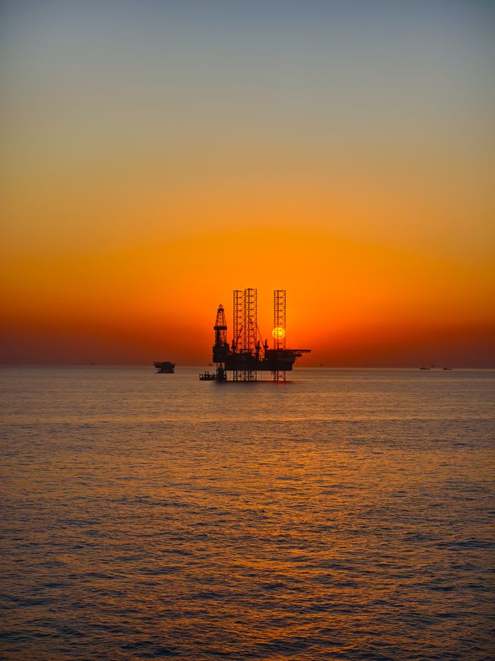 gallery-05 Silhouette of an oil rig against a vibrant sunset over the ocean, capturing the essence of industrial beauty.